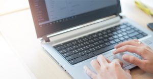 foto colorida de pessoa usando o computador com foco apenas nas mãos