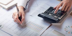 Pessoa preenchendo planilhas de cálculos e usando calculadora para estudo da prova do CFC.