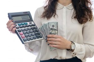 Mulher de branco segurando uma calculadora e notas de dinheiro, representando o patrimônio líquido de uma empresa.