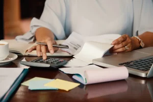 mãos de uma pessoa mexendo numa calculadora, segurando uma caneta e provavelmente analisando um fato contábil