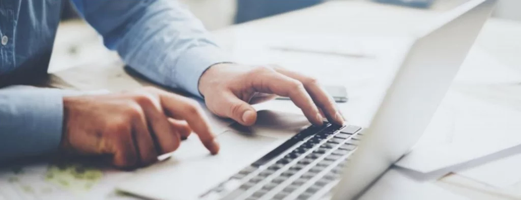 Imagem de mãos usando notebook sobre uma mesa, a pessoa de camisa azul, ilustrando pesquisa no Diário Oficial Amazonas.